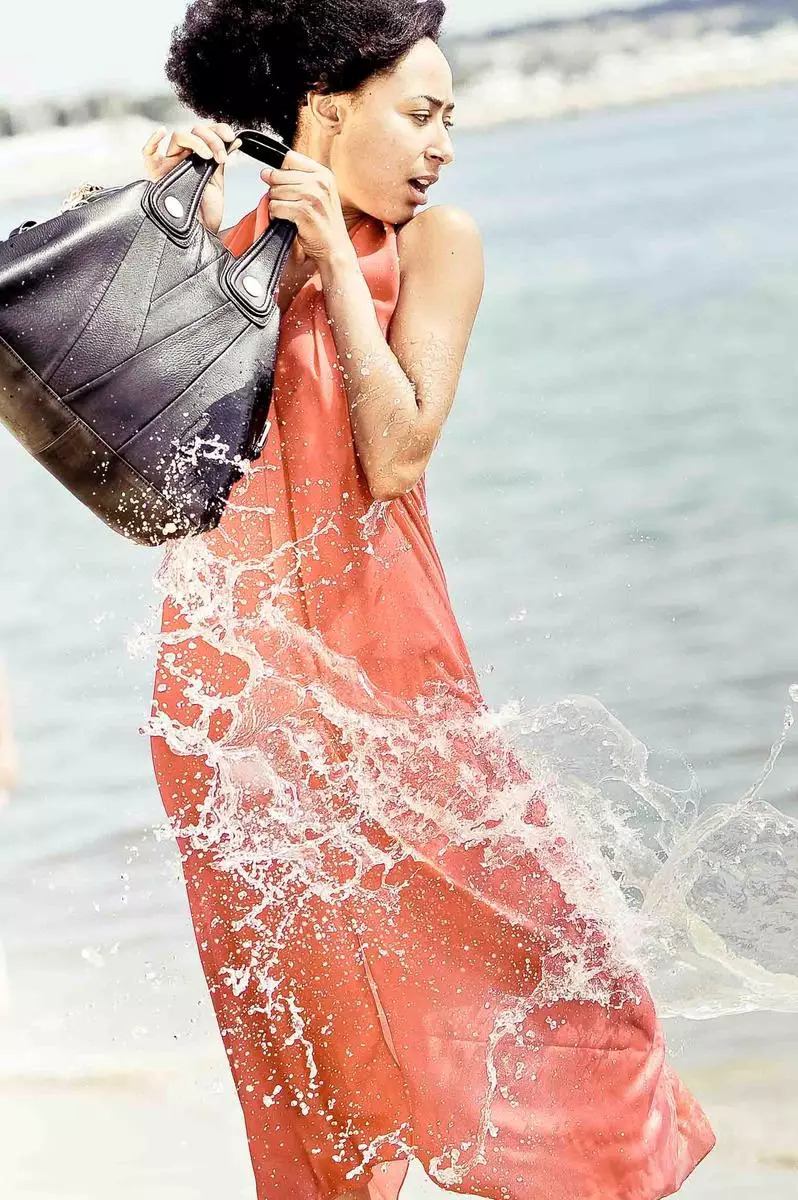 book photo studio à Lyon, Portrait d'une femme sur la plage tenant un sac à main et se faisant arroser