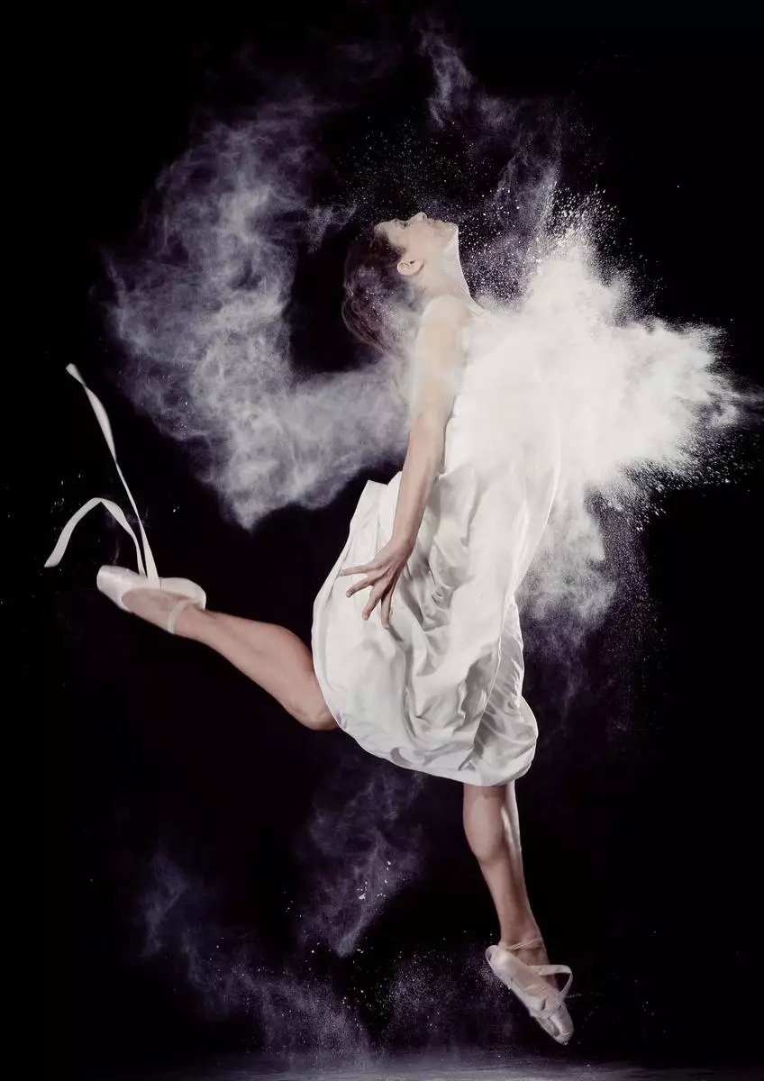 Danseuse de ballet en body noir saute haut et danse avec de la farine sur la